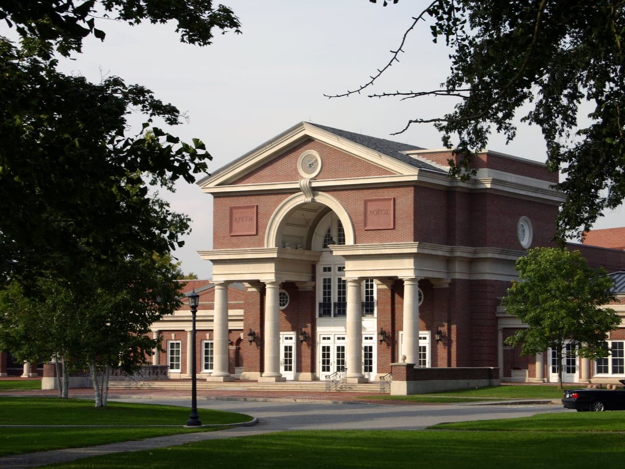 The Main Building at the Hotchkiss School, a brick building with a columned portico and a clock in its pediment, framed by trees