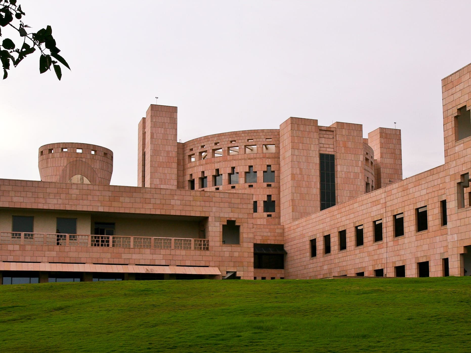 Pink sandstone buildings with a round tower and square windows above a green lawn at the Indian School of Business in Hyderabad