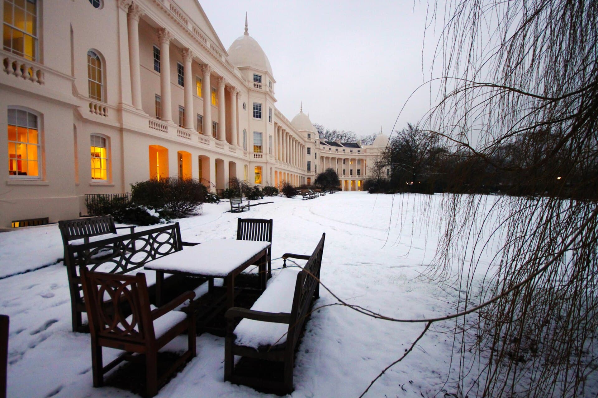The columned buildings of London Business School across a snowy garden at dusk