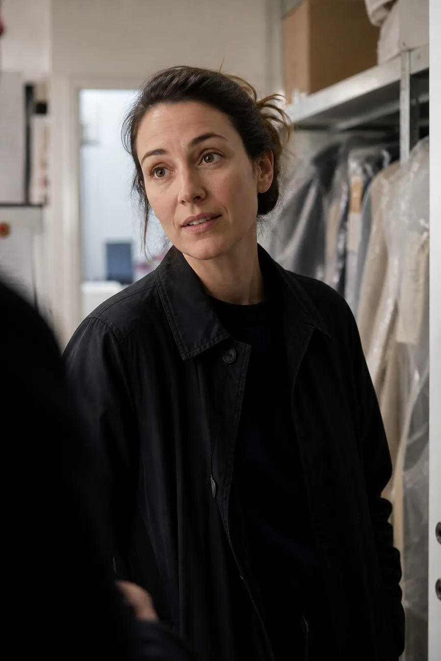 Illustration of a woman in a dark coat in a stockroom with garments on racks